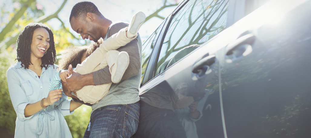 Father, mother and daughter standing beside a car.